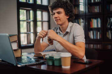 Fototapeta premium Young student eating a snack while studying in the library