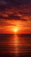 Obraz premium Golden sun dips below the horizon, painting the sky with fiery orange and red hues over the calm evening sea, reflecting on gentle waves near the coast