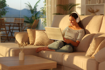 Obraz premium Happy woman with headphone at sunset using laptop