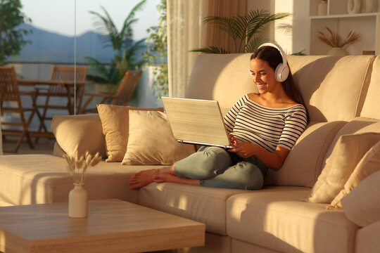Happy woman with headphone at sunset using laptop