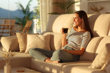 Happy woman laughing drinking coffee at sunset at home