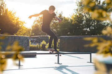A skateboarder performs a rail grind trick at a sunny skate park, showcasing balance and skill.