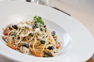 A plate of savory spaghetti is generously topped with grated Parmesan cheese, fresh parsley, cherry tomatoes, and black olives