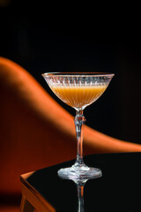 Stylish cocktail in crystal glass on black reflective table in moody bar