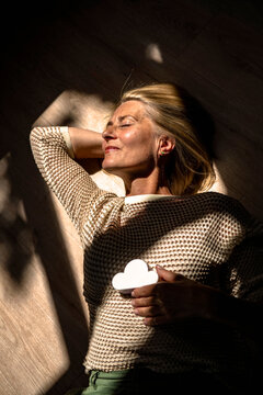 Smiling mature woman resting on floor with cloud model at home