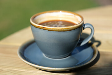 Cup of black coffee on wooden table in garden, closeup view