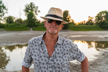 portrait of a smiling middle-aged man wearing a panama summer hat and sunglasses on the riverbank...