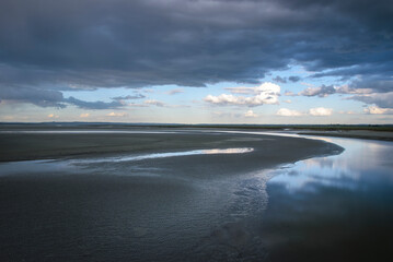 Calm waters reflect dramatic clouds over a winding shoreline at twilight