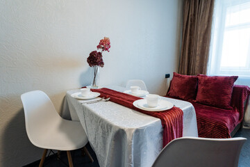 This cozy living room features a neatly arranged dining table with comfy chairs and a stylish red couch, adding vibrant character and enhancing the spaces overall allure