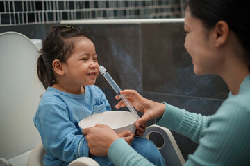 mother making nasal wash for happy toddler girl with syringe and saline. cleaning nose