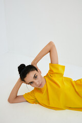 Young woman lying on white floor wearing bright yellow shirt, showing relaxed pose with hand behind...