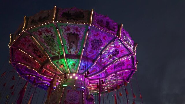 Rotating vintage carousel in blue hour with colourful neon lights. Traditional Bavarian carnival theme park at the Kiliani Summer Festival in W&uuml;rzburg, Germany. Close-up of carousel ride from below.