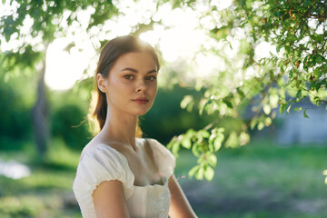Young woman in a white dress with soft sunlight filtering through green leaves, capturing the...