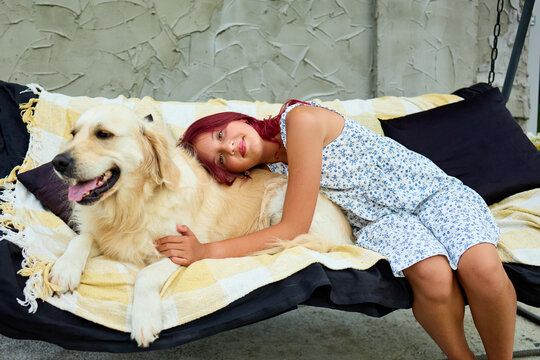 Relaxing outdoors, a teen girl enjoys a cozy moment with her beloved pet golden retriever on a warm day