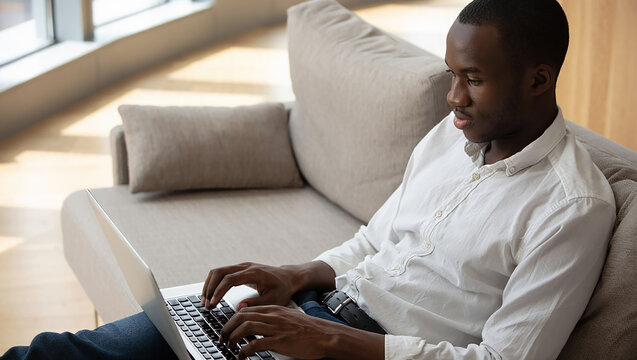 Focused Man Working on Laptop While Relaxing on Comfortable Couch at Home