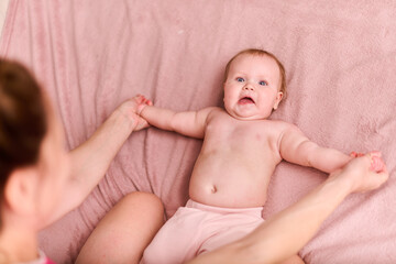 Young mother with infant girl on pink blanket. Warm lighting highlights moment. Baby lies on back,...