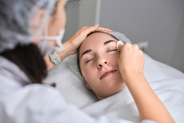 Young female receives relaxing facial treatment in contemporary spa. Calm and tranquility, focusing...