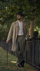 Man in vintage outfit walks by a wrought iron fence under trees. Concept of staged emotional...