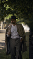 Vintage-dressed man walks under trees on a sunlit sidewalk. Concept of artist residencies and...
