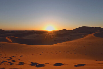 Sunset over the desert landscape, with its sand dunes stretching towards the horizon, embodies the tranquility of nature