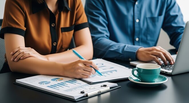 Two professionals collaborate on financial reports with a laptop and coffee highlighting teamwork and data analysis - Powered by Adobe