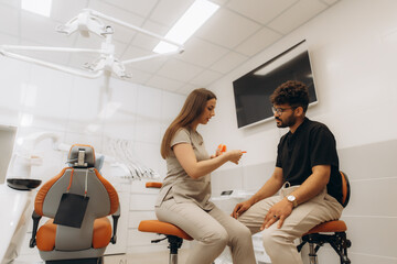 Naklejka premium Dentist showing teeth model to patient in modern clinic