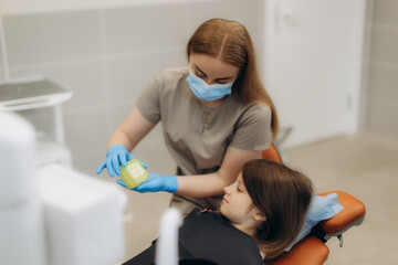 Dentist showing dental mold to young girl in clinic. Dentist shows aligners, braces, caps