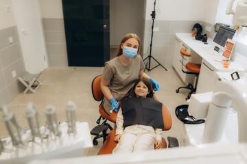 Dentist wearing surgical mask posing with young patient in dental clinic