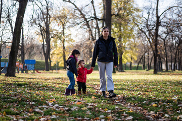 Mother walking with her two children in a park during autumn