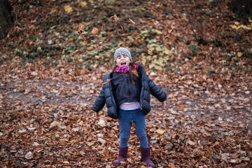 Happy girl playing with autumn leaves in a forest