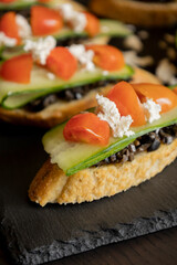 close up stock photo of greek-style crostini topped with olive paste, cucumber slices, cherry tomatoes, and feta cheese