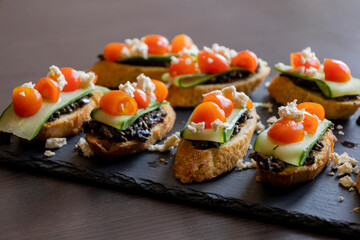 close up stock photo of greek-style crostini topped with olive paste, cucumber slices, cherry tomatoes, and feta cheese