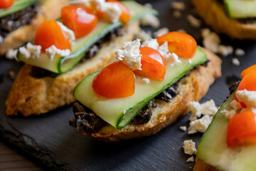 close up stock photo of greek-style crostini topped with olive paste, cucumber slices, cherry tomatoes, and feta cheese