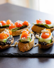 close up stock photo of greek-style crostini topped with olive paste, cucumber slices, cherry tomatoes, and feta cheese
