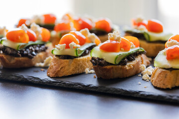 close up stock photo of greek-style crostini topped with olive paste, cucumber slices, cherry tomatoes, and feta cheese