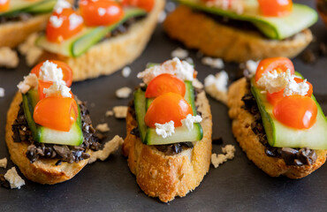 close up stock photo of greek-style crostini topped with olive paste, cucumber slices, cherry tomatoes, and feta cheese
