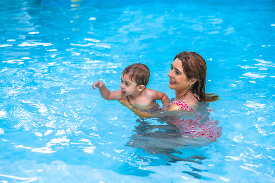 Mother teaching baby to swim in a blue pool