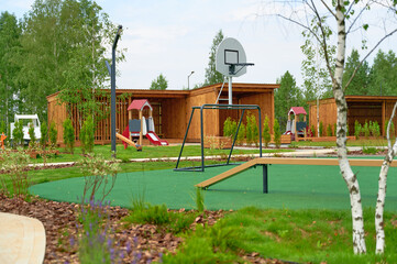 modern outdoor playground with slides, basketball hoop, lush greenery, and wooden shelters offers...