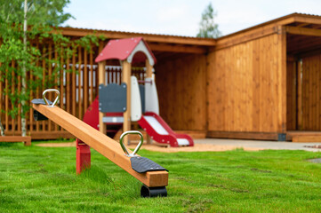 outdoor playground seesaw beside wooden playhouse. vibrant, inviting space designed for children’s play and adventure. features green grass, modern amenities for engaging outdoor fun