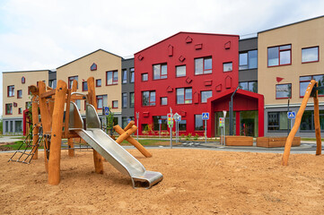 modern playground equipment near colorful school building. vibrant facade design with sand-covered...