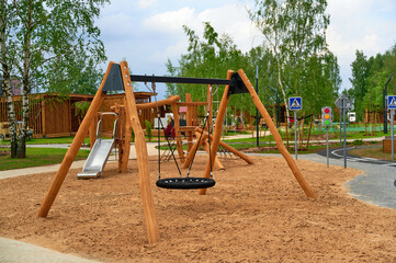Fototapeta premium modern playground features wooden swings and slides with sand surface. surrounded by green trees and walking paths, ideal for family outings and children's activities in urban parks.