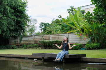 Young woman meditating outdoors by the pond in lush green garden