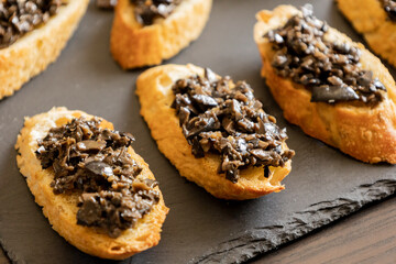 close up stock photo of greek-style crostini topped with olive paste. rustic party appetizer or mediterranean finger food