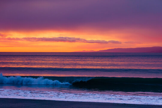 Sunset over the Strait of Juan de Fuca, orange sky reflecting on the waves coming to shore.
