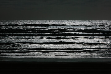Abstract black and white effect, breaking waves and overcast sky at night.