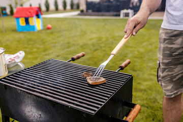 Close up of a hand holding grilling fork and grilling delicious piece of meat on a grill.