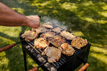 Close up of a hand grilling delicious meat on a grill in backyard.