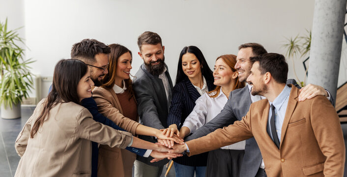 Leadership team stacking hands and smiling at each other at corporate office.