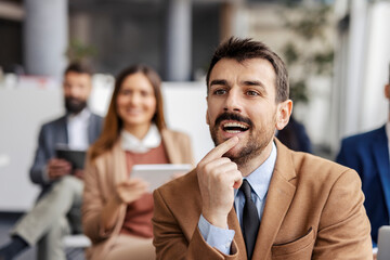 Portrait of focused businessman sitting on seminar and listening to presentation.