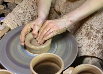 Hands of young potter working with clay and making vase or pot, jug or mug. Throwing pottery on...